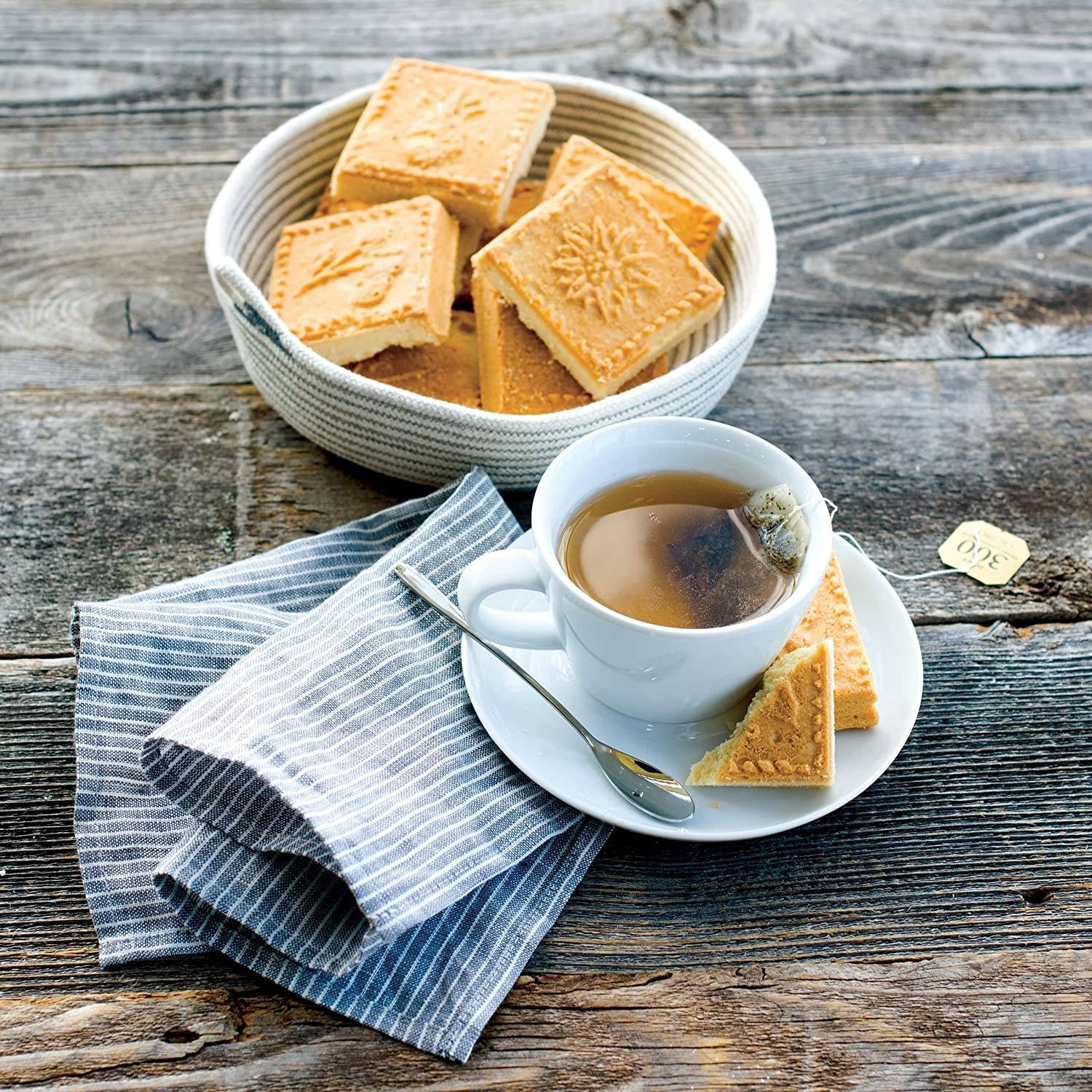 Cup of tea with shortbread cookies embossed with floral designs in white bowl on rustic wooden table