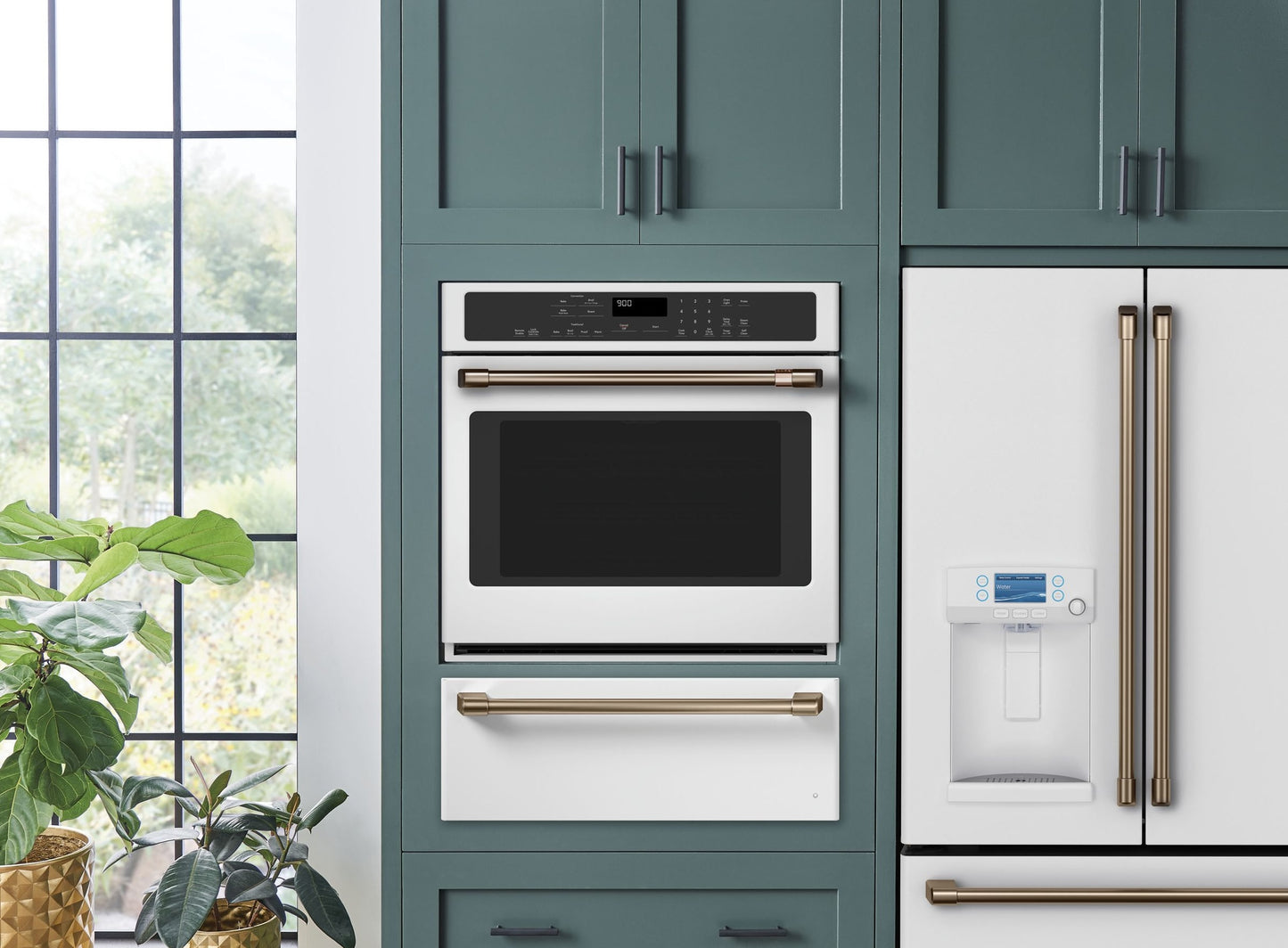 Built-in white oven with digital display and gold hardware integrated into teal cabinetry in modern kitchen setting.