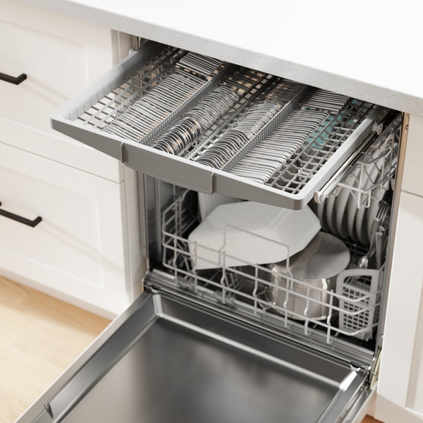 Open dishwasher with top silverware rack and bottom racks holding plates and kitchenware in modern kitchen setting