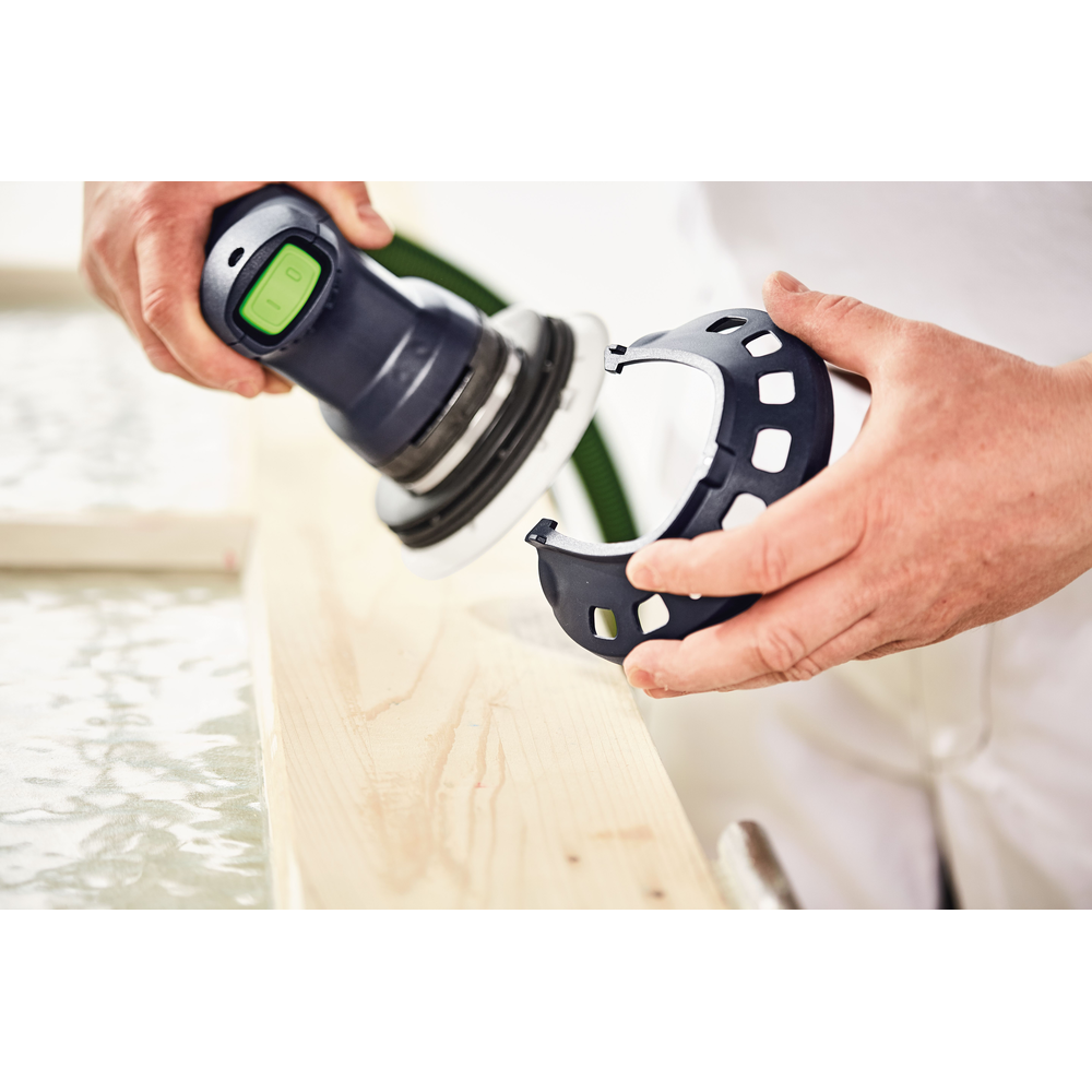 Hands attaching a sanding guard to a Festool random orbit sander over a wooden plank for woodworking tools use