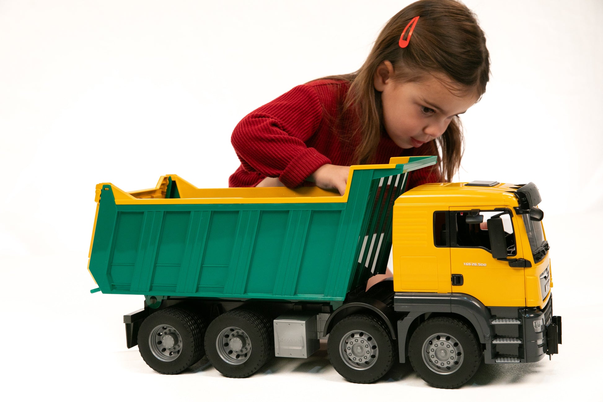 Child playing with detailed yellow and green Bruder Man Dump Truck toy on white background