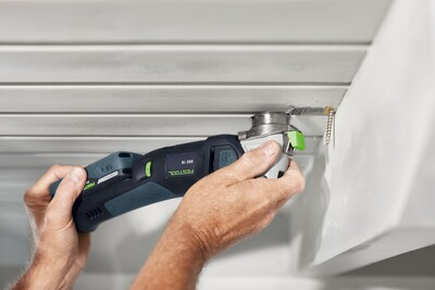 Person using a Festool oscillating saw blade to cut or remove material near a drywall corner in a home improvement project