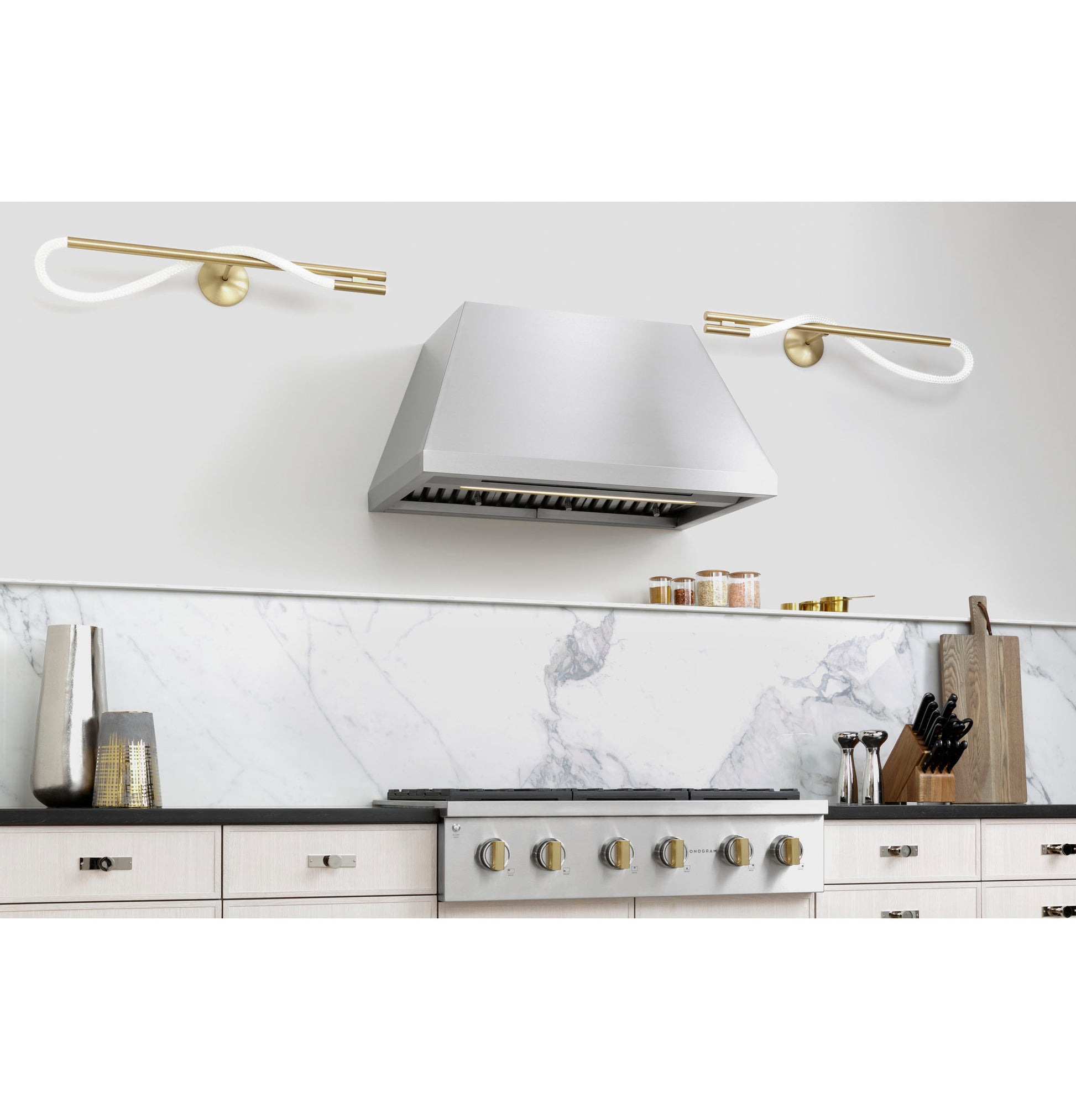 Stainless steel professional hood above gas cooktop with marble backsplash and modern kitchenware accessories