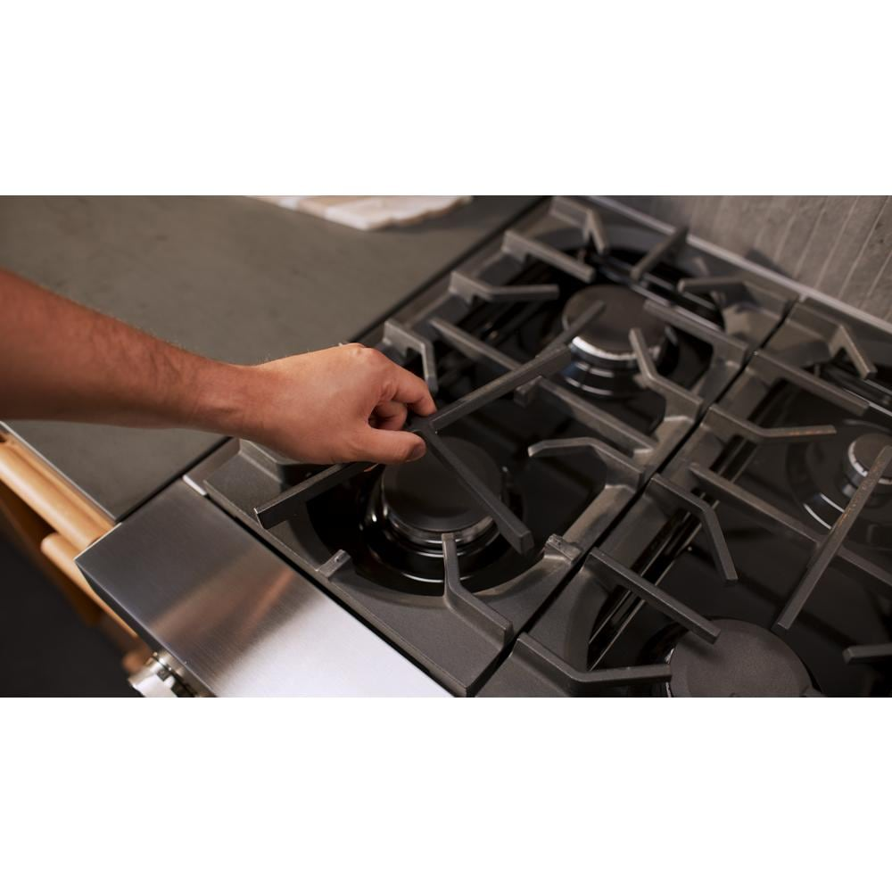 Hand adjusting cast iron grate on stainless steel 36-inch gas range burner in modern kitchen setting