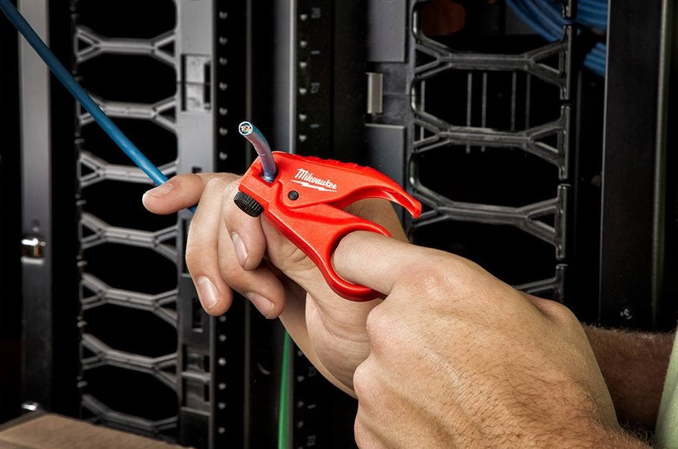 Hand using a red Milwaukee tool to strip insulation from a blue twisted pair cable in a server rack setting