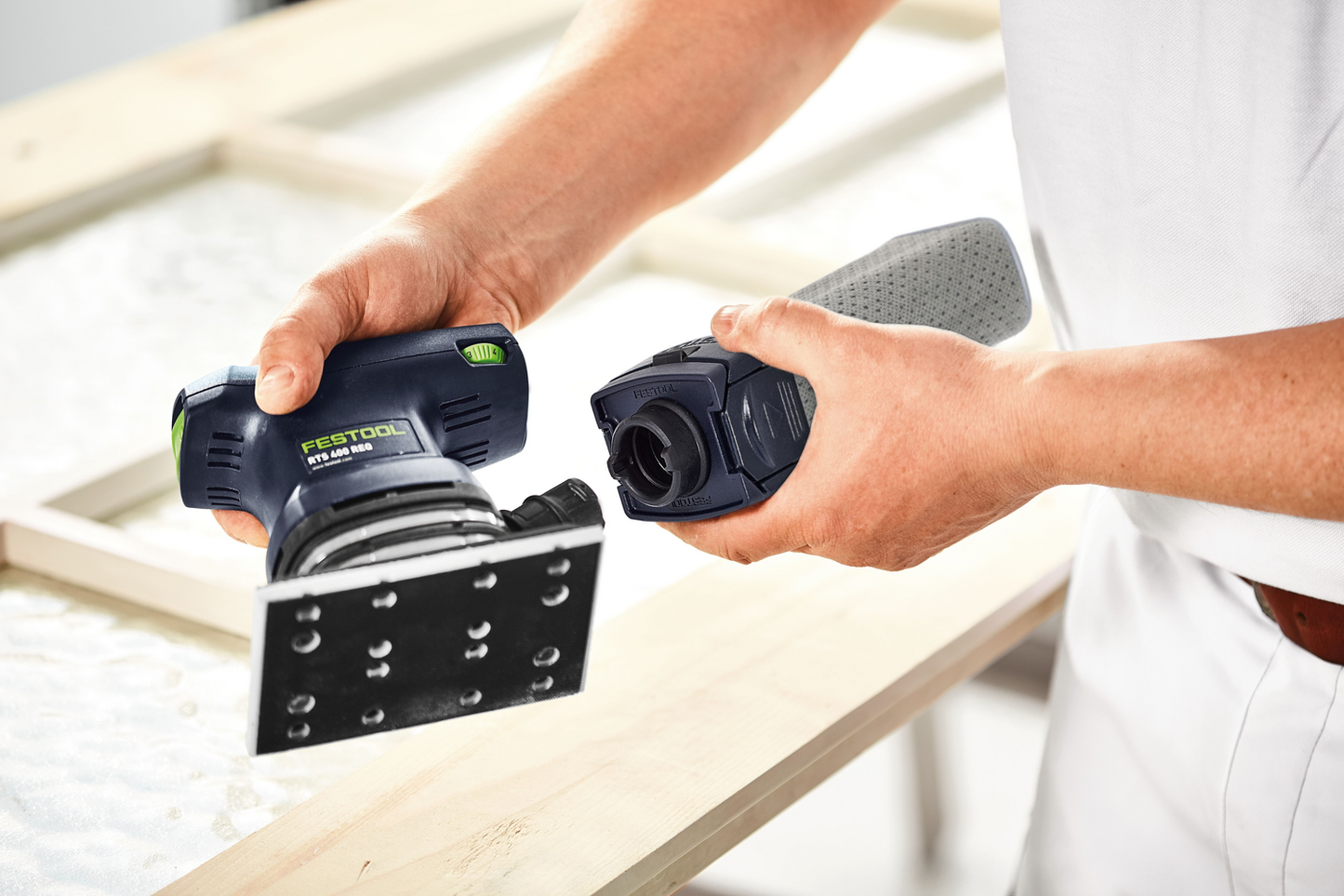 Person attaching dust collection container to blue and black orbital finish sander for woodworking projects