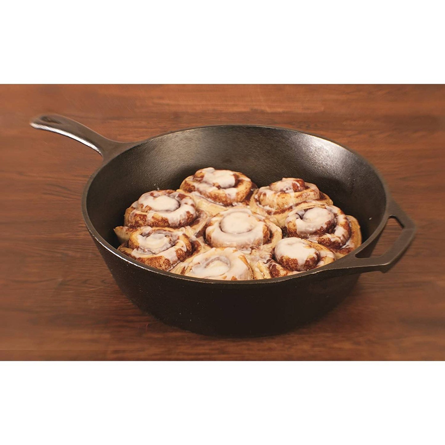 Seasoned cast iron deep skillet holding freshly baked cinnamon rolls with icing on wooden surface in kitchenware collection