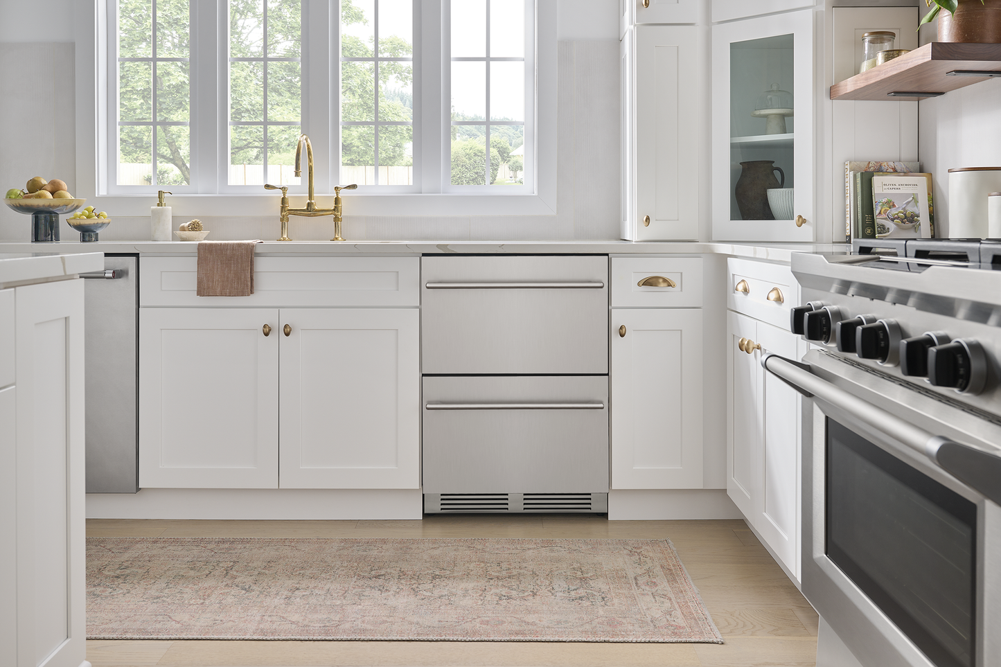 Built-in stainless steel under-counter refrigerator drawer integrated in modern kitchen with white cabinetry and gold fixtures