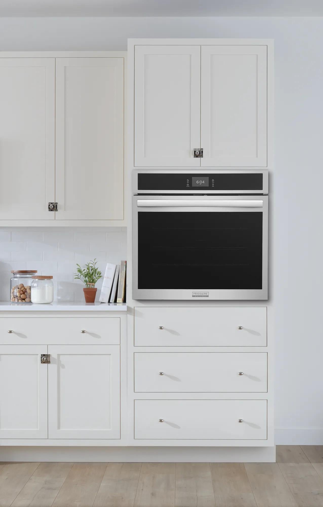 Built-in stainless steel electric wall oven with digital display, installed in white kitchen cabinetry with drawers below.
