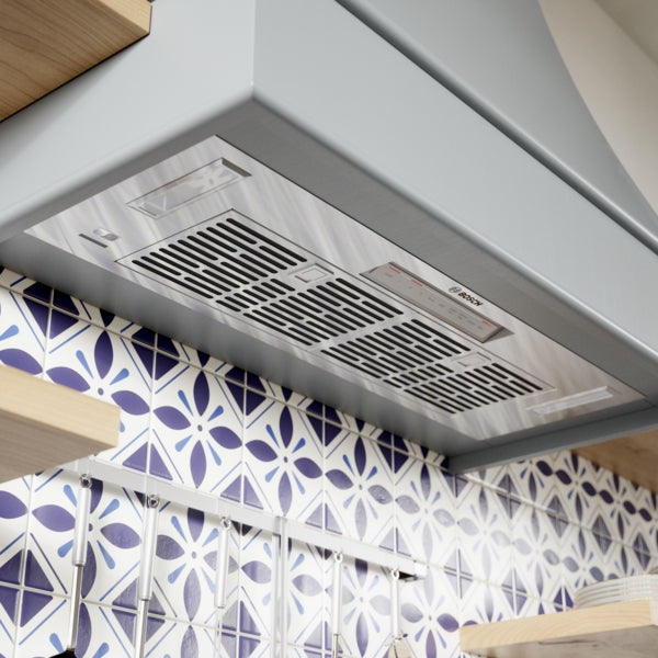 Under-cabinet stainless steel custom insert vent with control panel, installed above kitchen backsplash tiles in home improvement setting