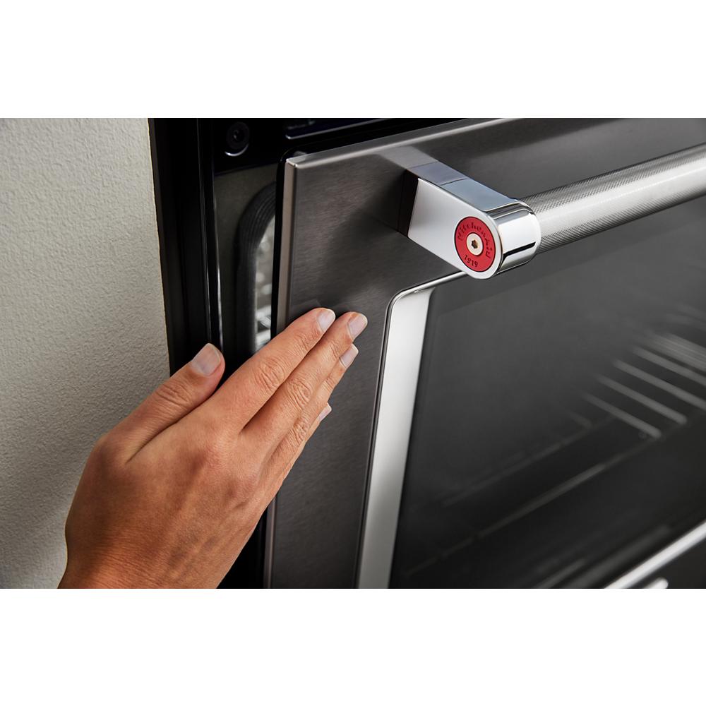 Hand reaching to open stainless steel single wall oven door in modern kitchen appliance setting