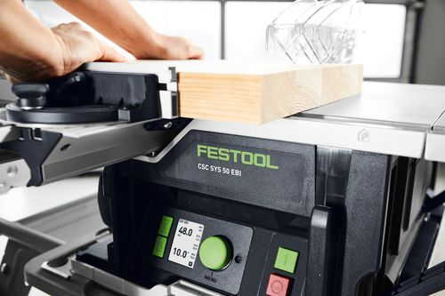 Person pushing a wood board through a Festool cordless table saw with digital display and adjustable fence in workshop