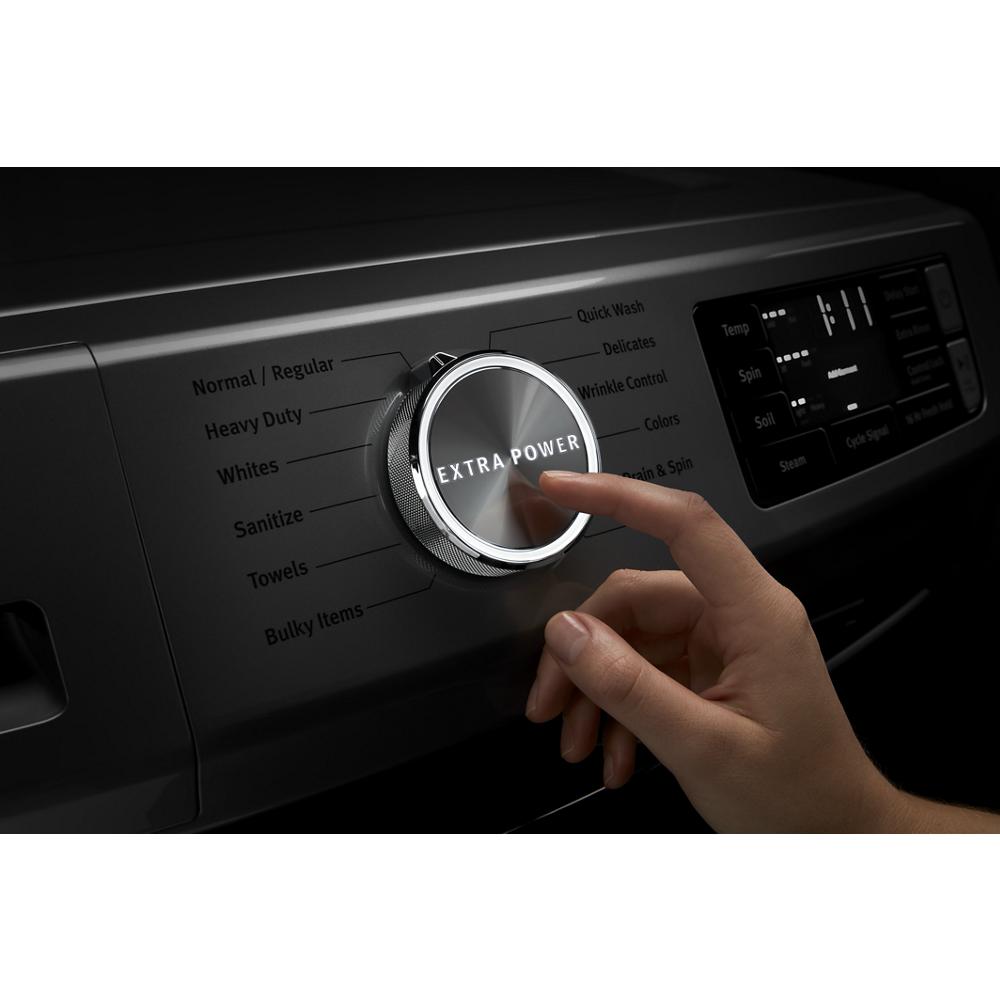 Hand pressing the metallic dial labeled Extra Power on a black front load washer control panel in appliances collection