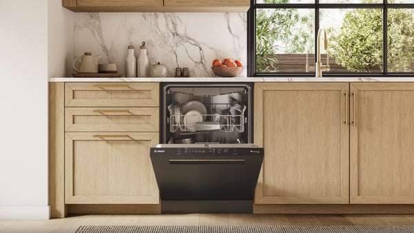 Open black 24-inch dishwasher integrated into light wood kitchen cabinetry with marble backsplash and window view