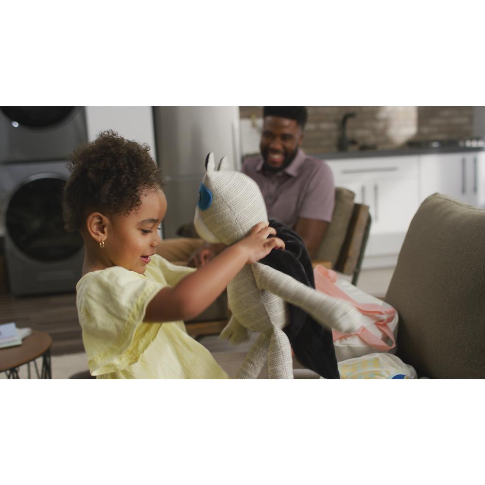 Child playing with stuffed animal on sofa in living room with laundry appliances in background