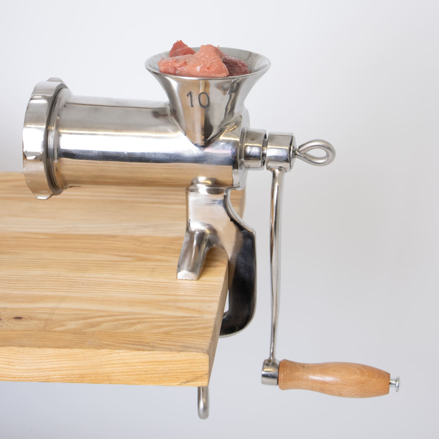 Clamp-down manual meat grinder with wooden handle secured on wooden table for kitchen gadgets and small appliances