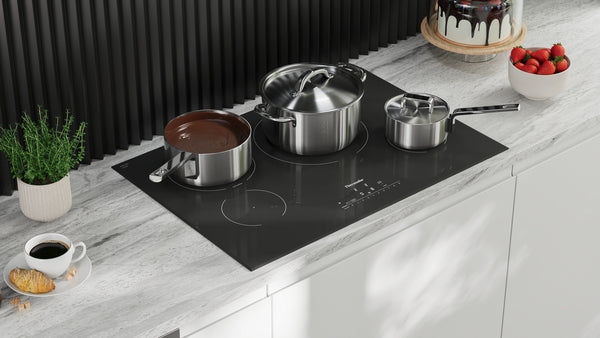 Black induction cooktop with three stainless steel pots on white marble countertop in modern kitchen setting