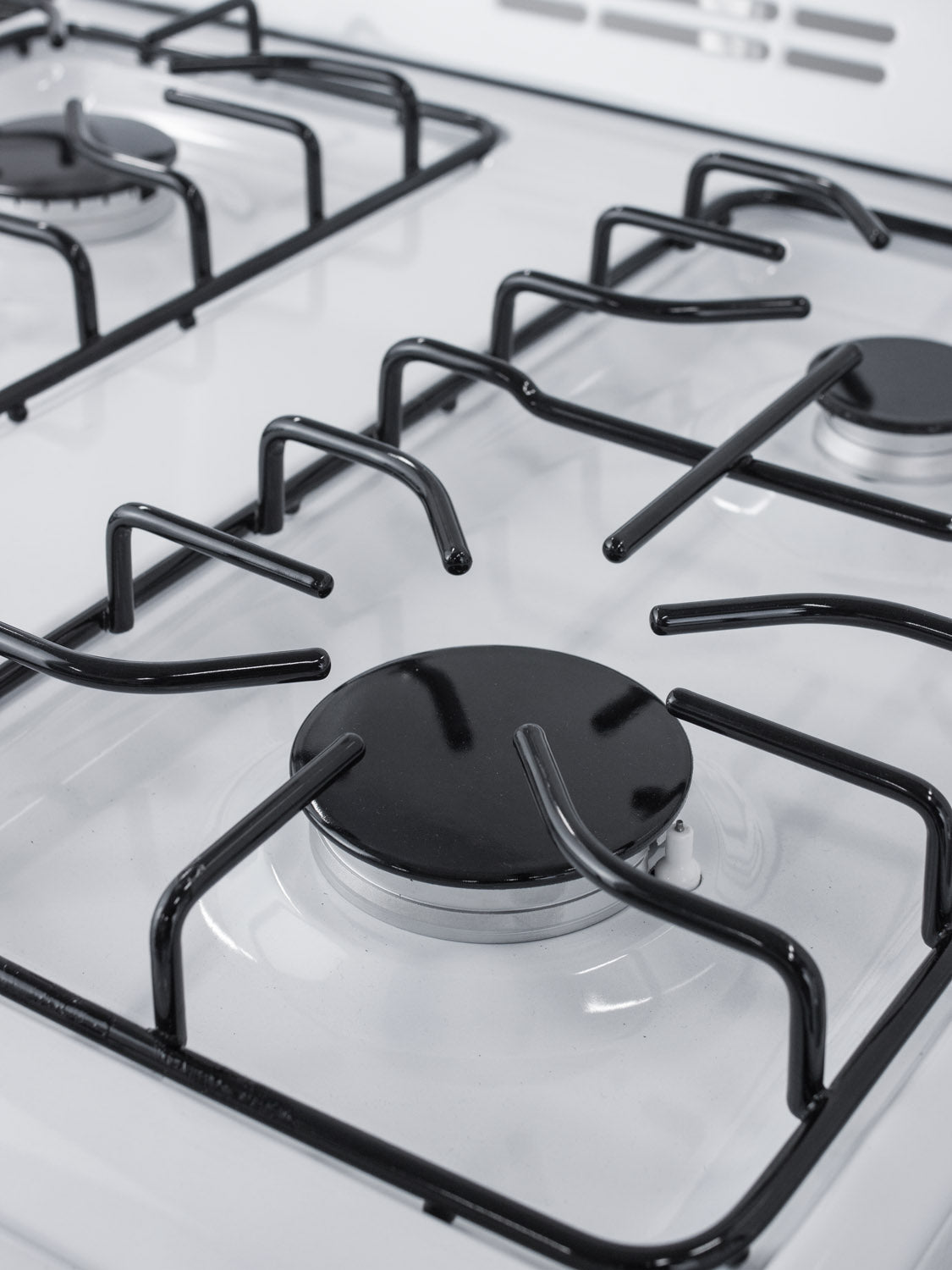 Close-up of black metal burner grates and gas burners on a slim white cooking range from Ranges & Cooktops collection