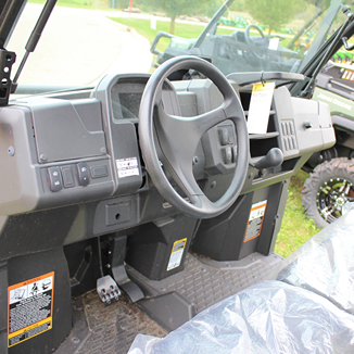 Interior view of utility vehicle cabin showcasing steering wheel, control panel, and textured floor designed for rugged use
