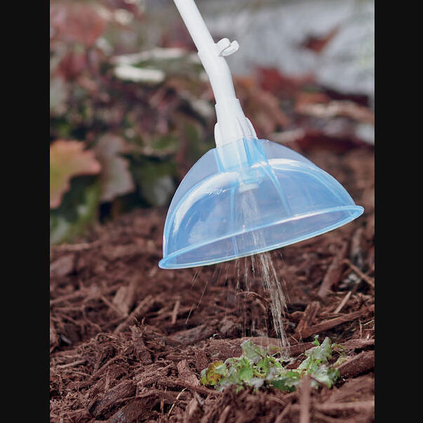 Close-up of blue weed killer sprayer wand applying product to small weeds in mulch for home garden care