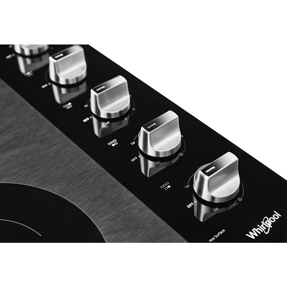 Close-up of brushed metal control knobs on black ceramic glass cooktop from Whirlpool kitchen appliances collection