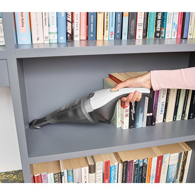 Person using white and gray cordless handheld vacuum to clean inside bookshelf in a home setting