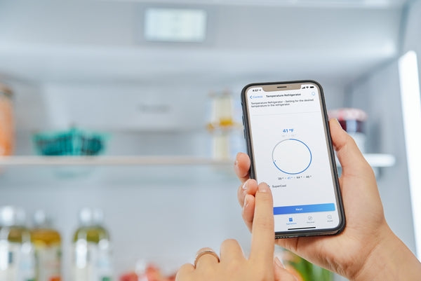 Hand holding smartphone inside refrigerator controlling temperature settings via app in Kitchen & Kitchenware collections