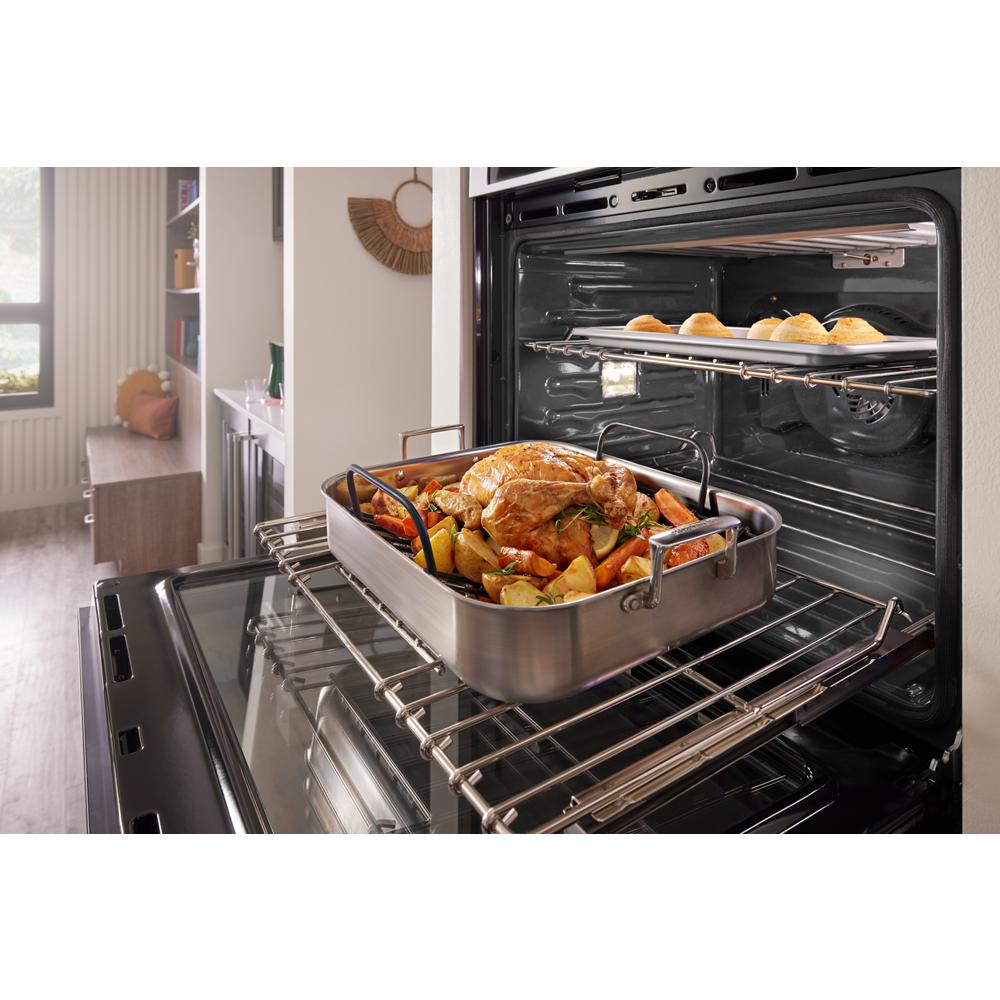 Stainless steel oven with roasted chicken and vegetables on lower rack and baked rolls on upper rack in kitchen setting
