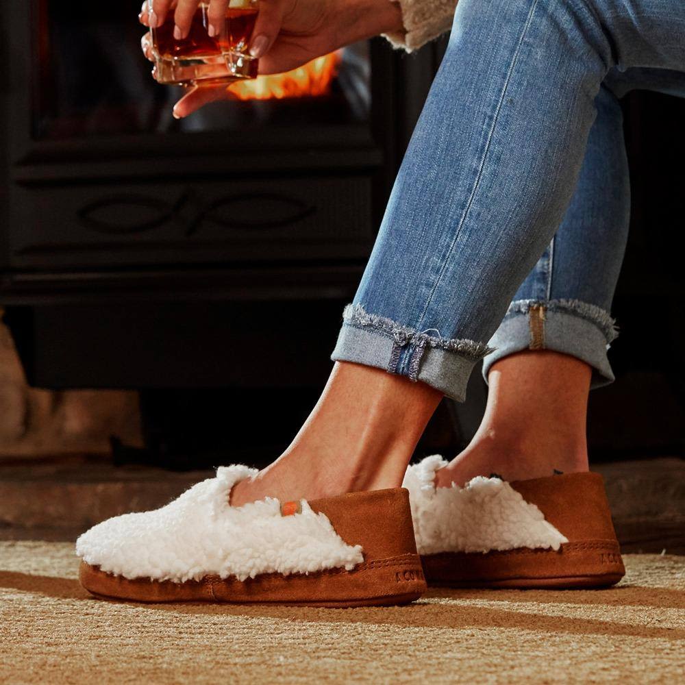 Women wearing medium buff moccasin slippers with soft popcorn texture and collapsible heel near fireplace holding a drink