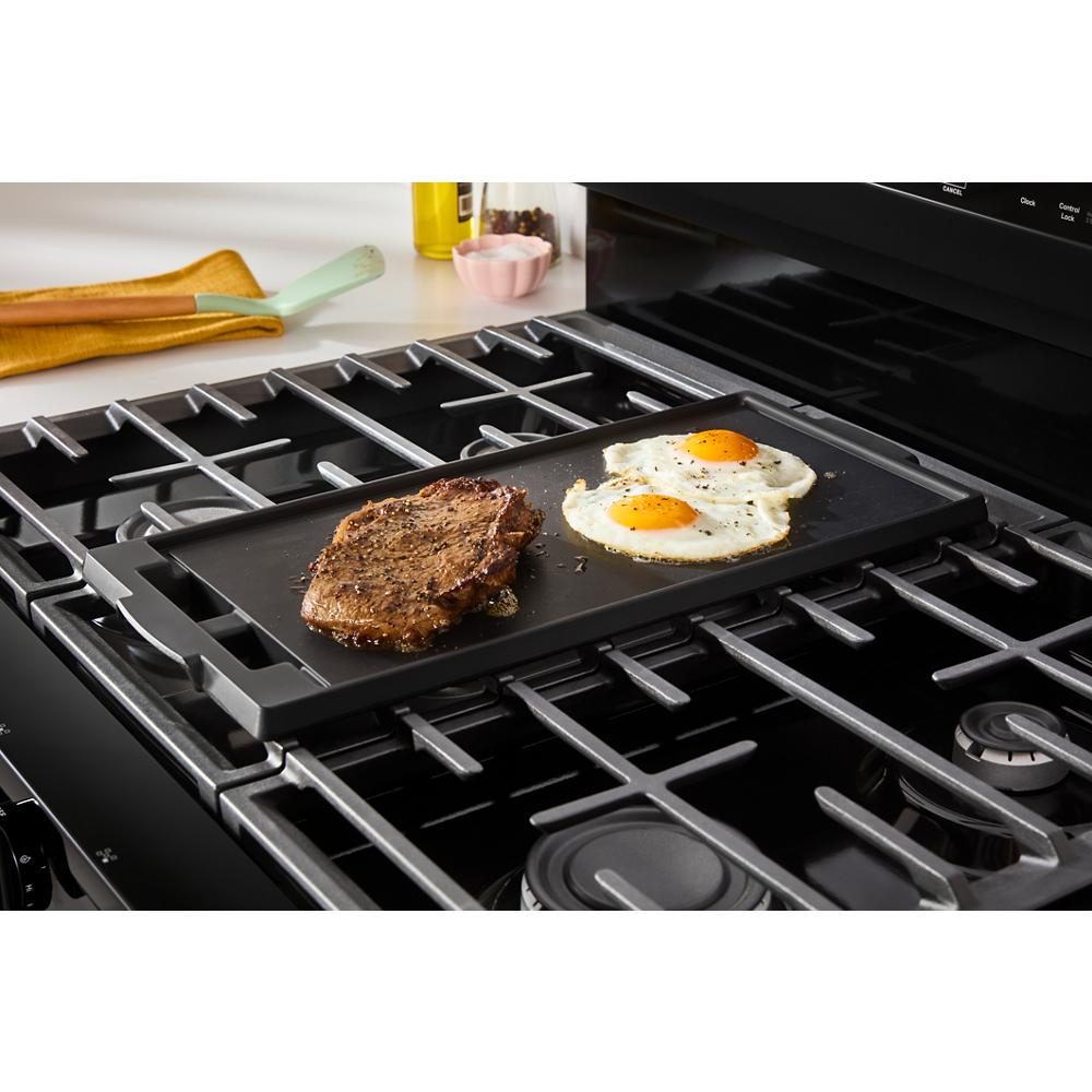 Black gas range with griddle cooking steak and sunny-side eggs in a kitchenware and appliances setting