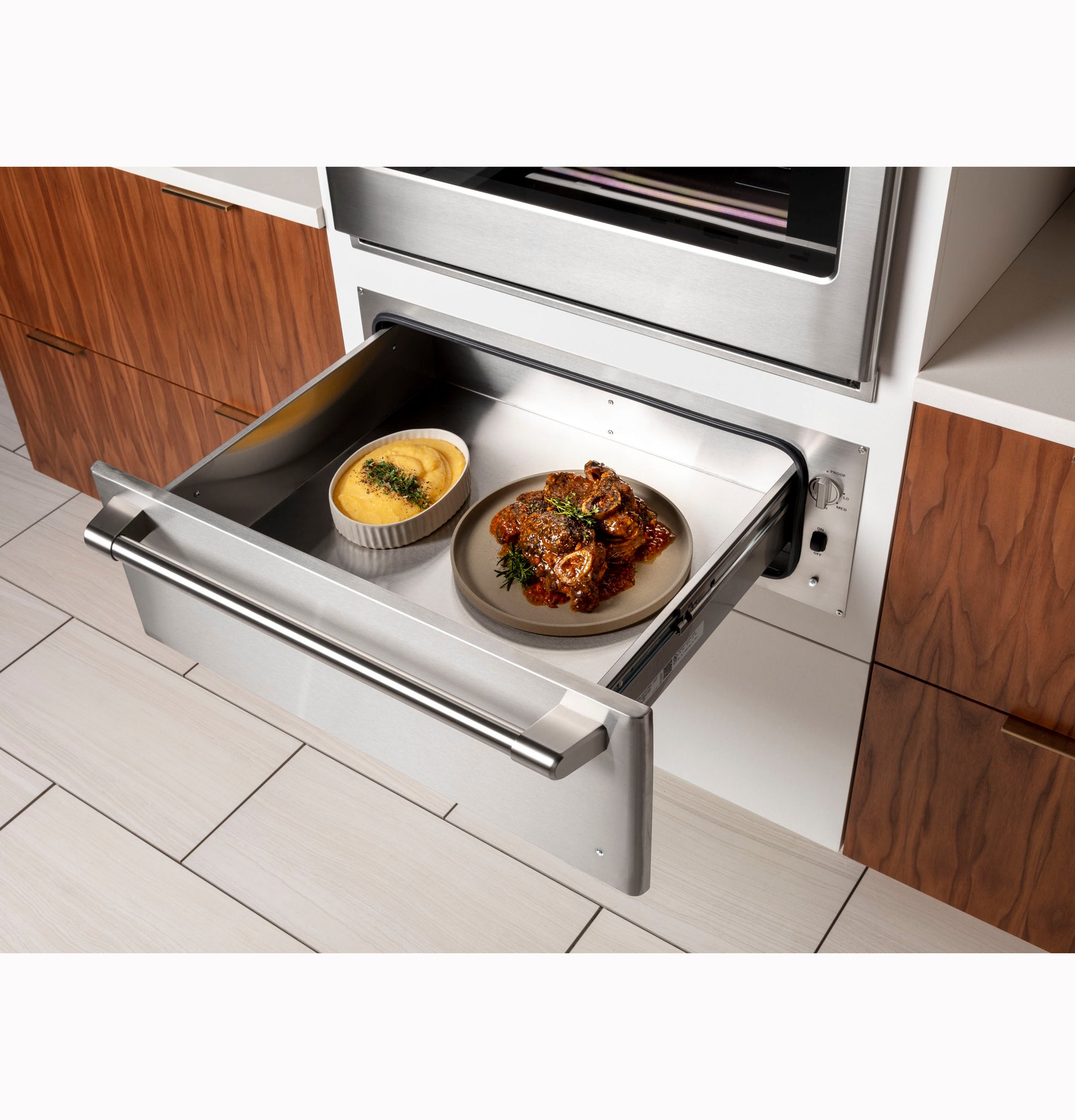 Open stainless steel warming drawer with cooked food inside in modern kitchen and wall ovens collection