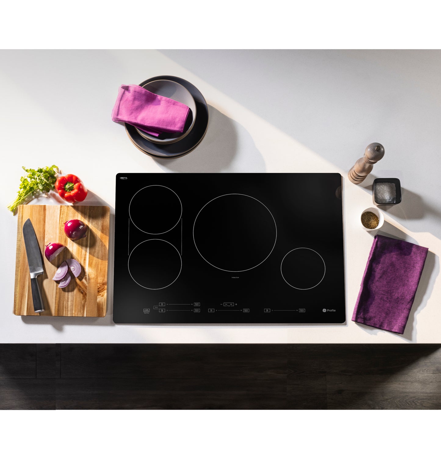 Black induction cooktop with four cooking zones and touch controls set in a modern kitchen countertop with fresh vegetables nearby