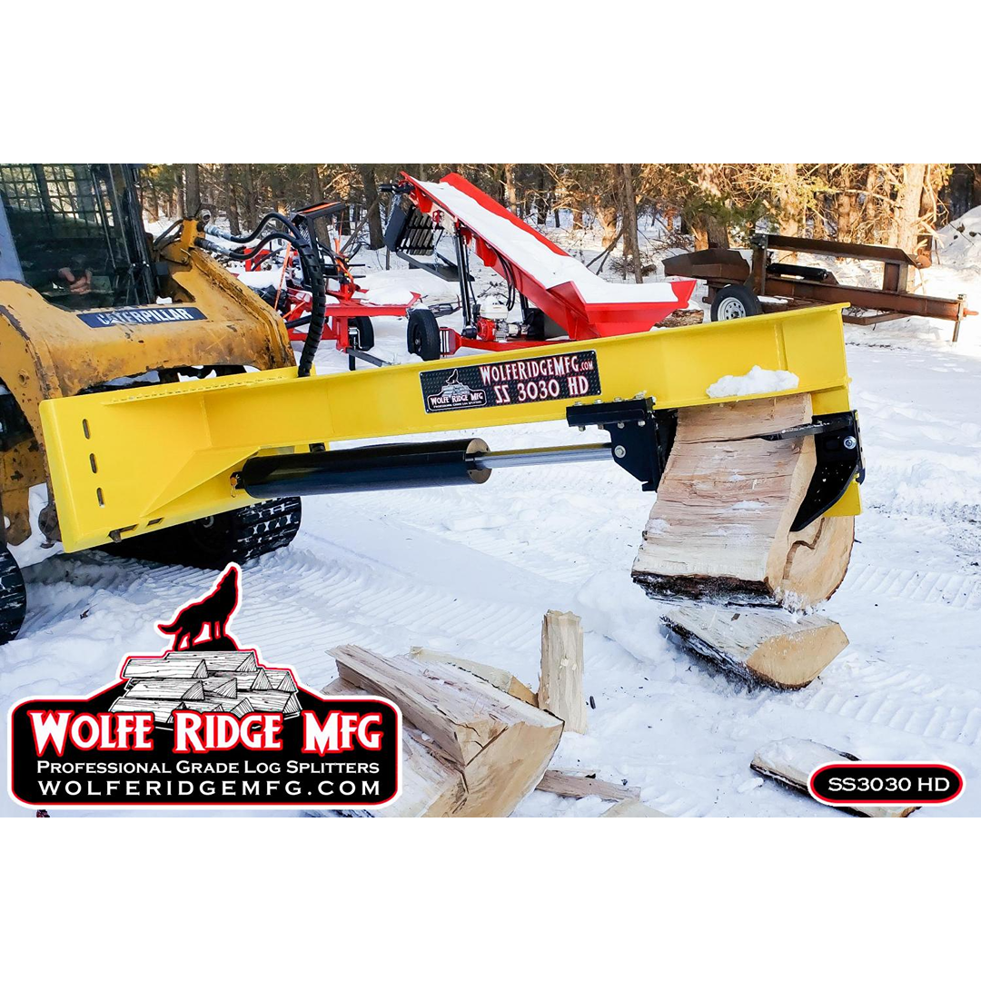 Yellow Wolfe Ridge skid steer attachment splitting large logs outdoors in snowy firewood processing area