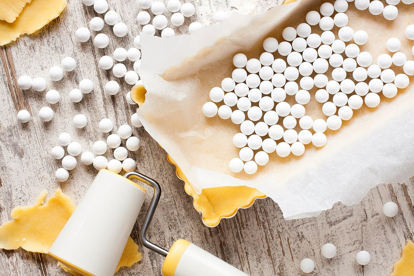 White ceramic pie weights on parchment paper in a baking dish with dough and roller for Kitchenware collection