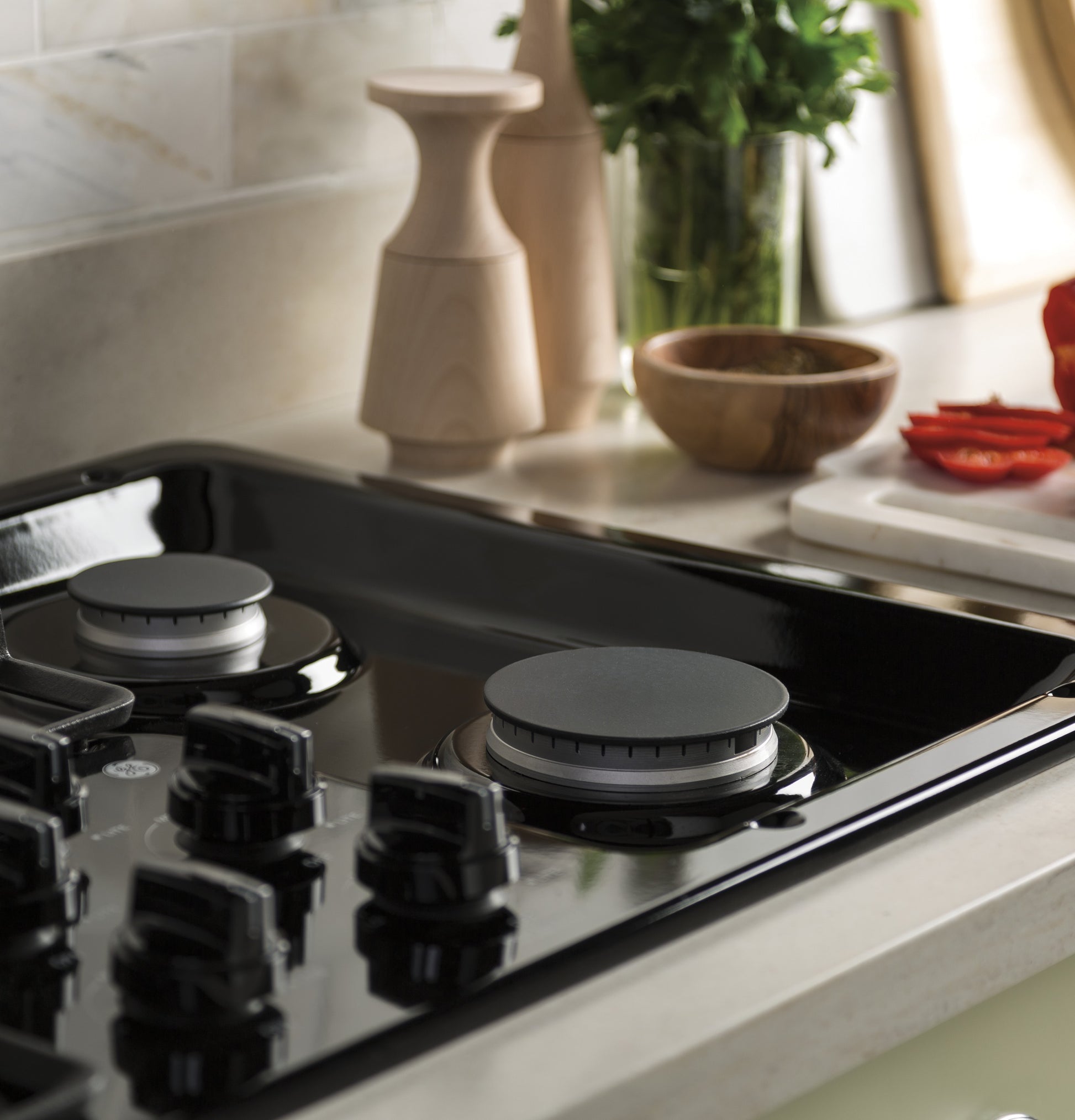 Close-up of black glass GE built-in gas cooktop with control knobs and dishwasher-safe grates in modern kitchen setting