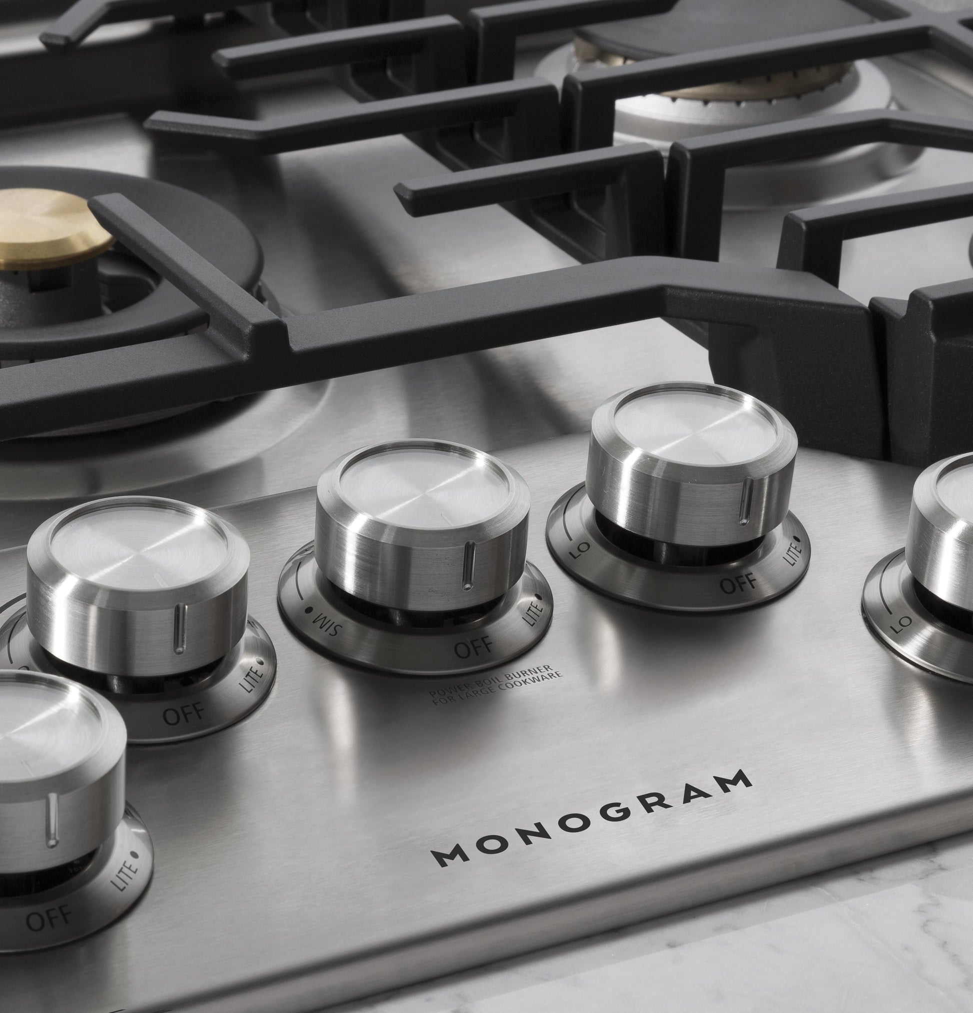 Close-up of stainless steel gas cooktop burner knobs with black grates on a deep-recessed model in kitchen appliances collection