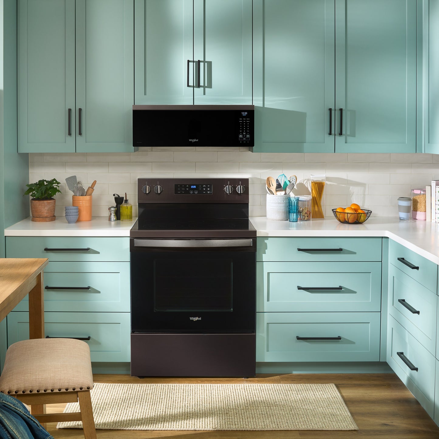 Modern kitchen featuring black Whirlpool microwave and stove surrounded by light blue cabinetry and white countertops