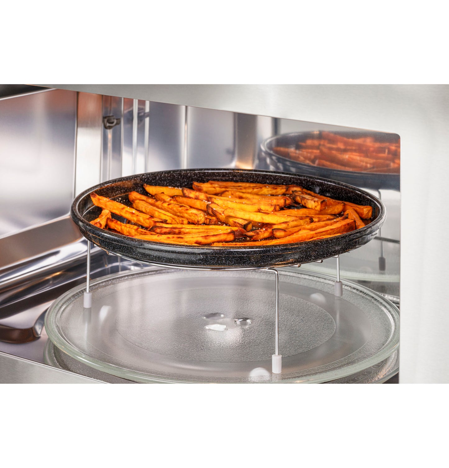 Over-the-range microwave interior with black tray cooking seasoned fries on elevated rack in kitchen appliances setting
