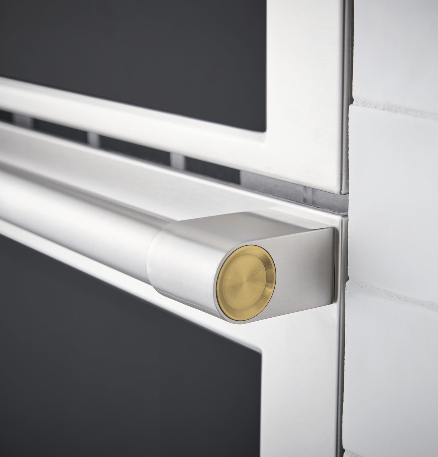 Close-up of stainless steel wall oven handle with gold accent on sleek modern kitchen appliance door panel