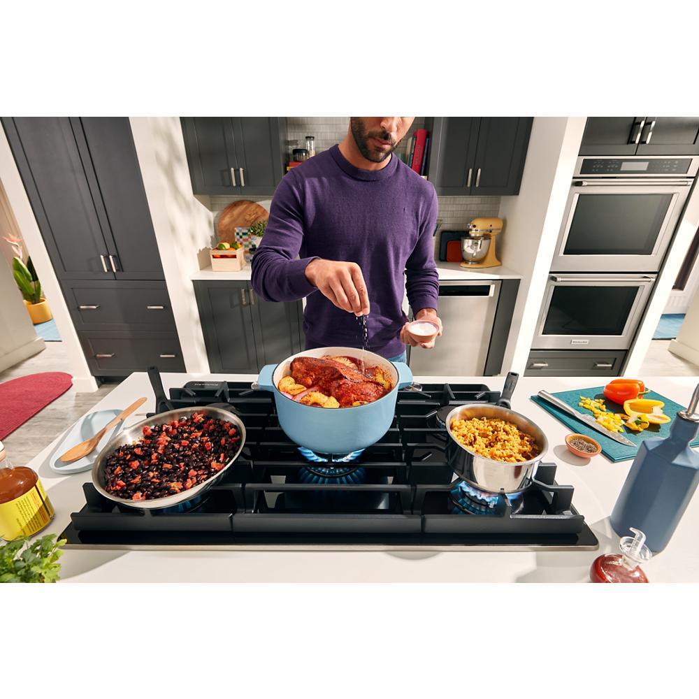 Person seasoning a large blue pot on a black 36-inch gas-on-glass cooktop in modern kitchen setting