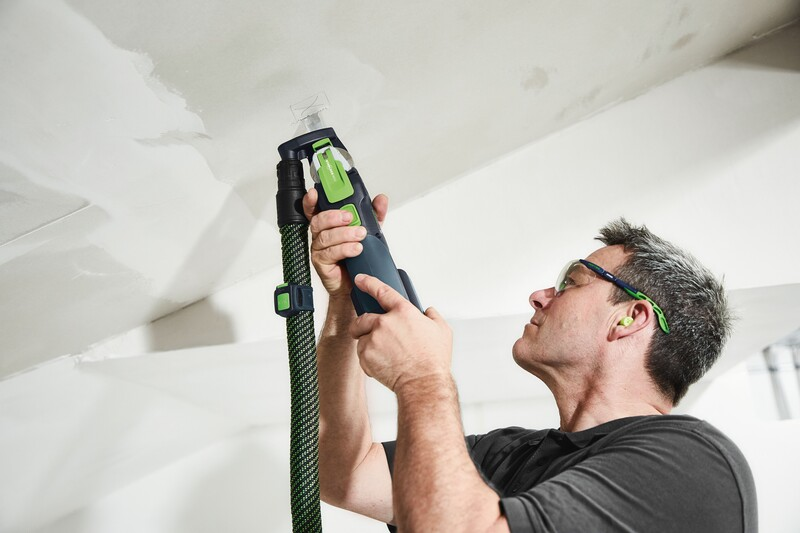 Man using Festool dust extraction device with green hose to sand ceiling surface during home improvement project
