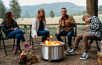 Four people enjoying an outdoor gathering around a stainless steel smokeless fire pit in a natural setting