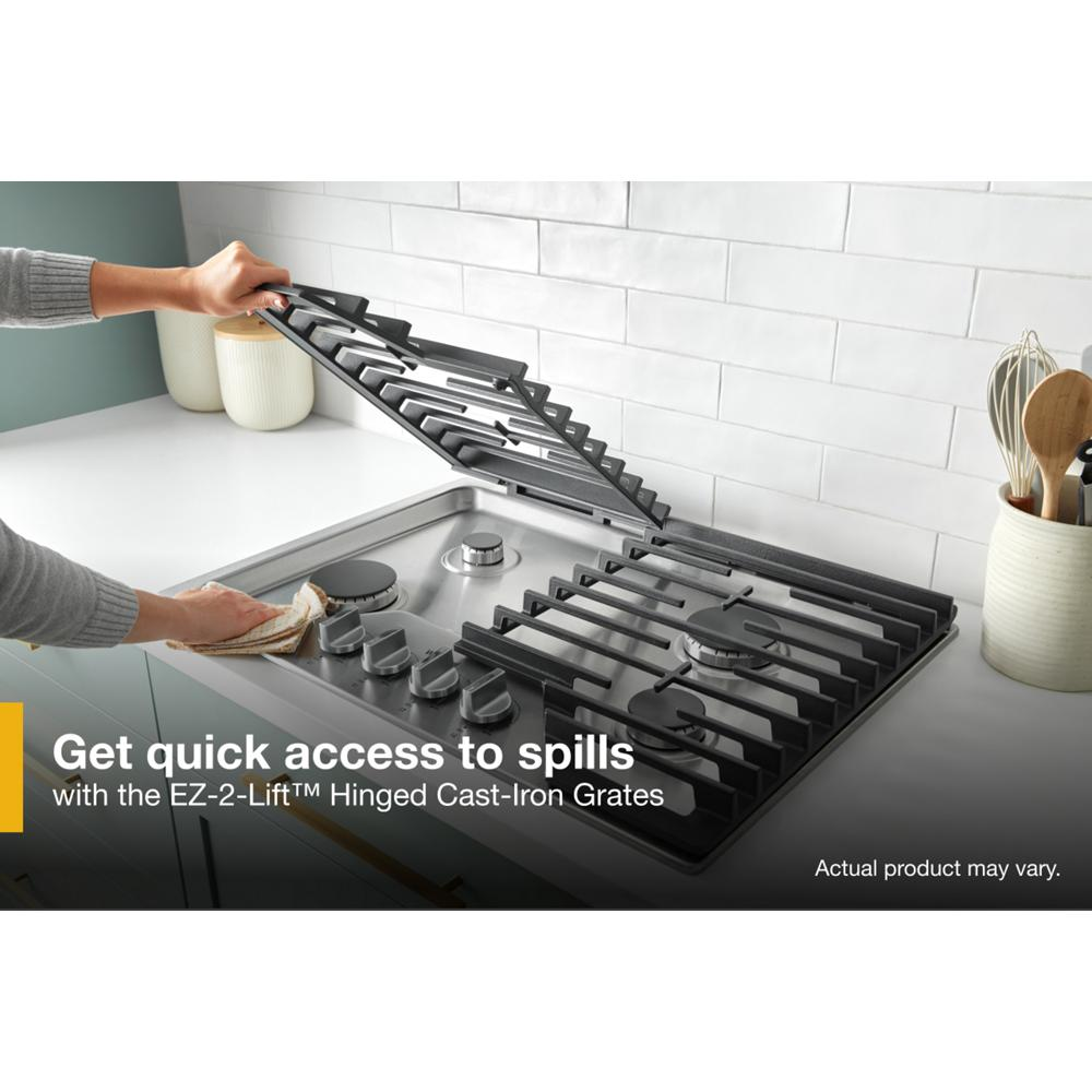 Person lifting hinged cast-iron grate on stainless steel 30-inch gas cooktop in modern kitchen setting