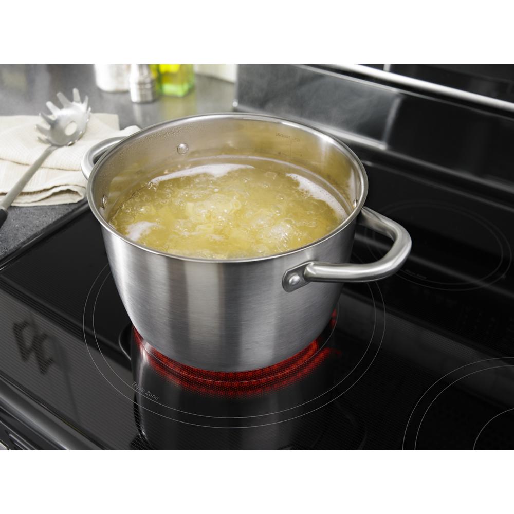 Stainless steel pot boiling water on glowing heating element of black electric induction cooktop range surface