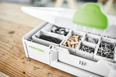 White modular organizer with clear lid and green latch holding various screws and wooden dowels for workshop use