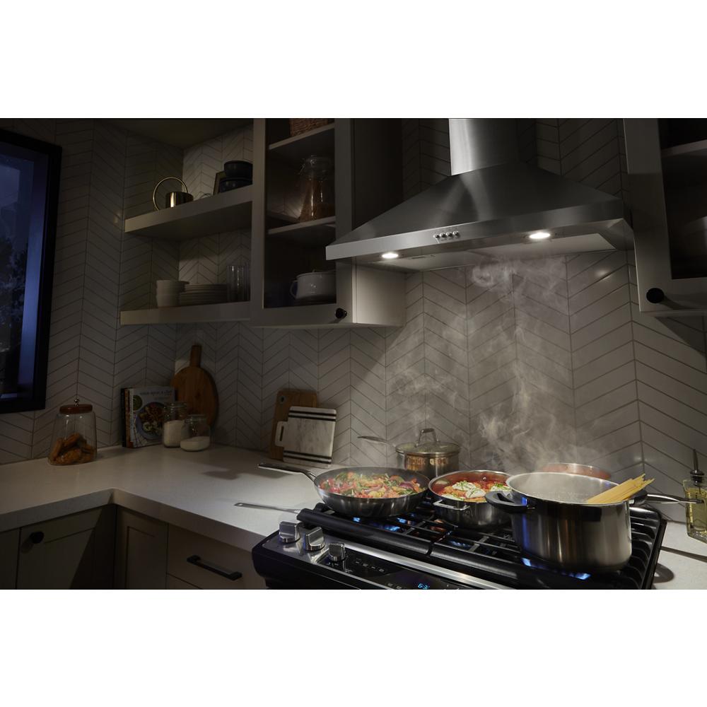 Stainless steel chimney wall mount hood venting steam over gas cooktop in modern kitchen and appliances setting