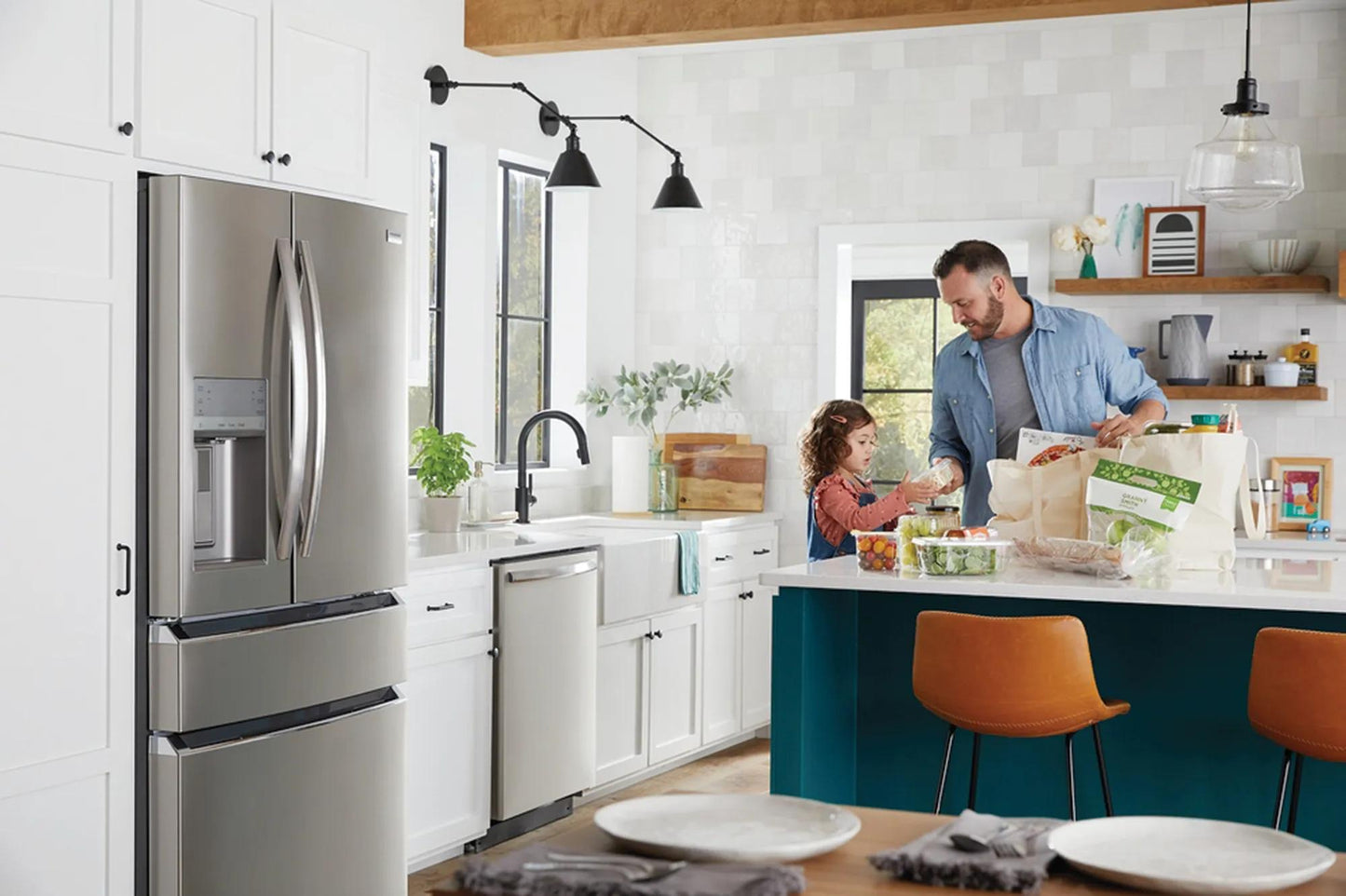 Modern kitchen with stainless steel dishwasher, white cabinets, island seating, and man with child unpacking groceries