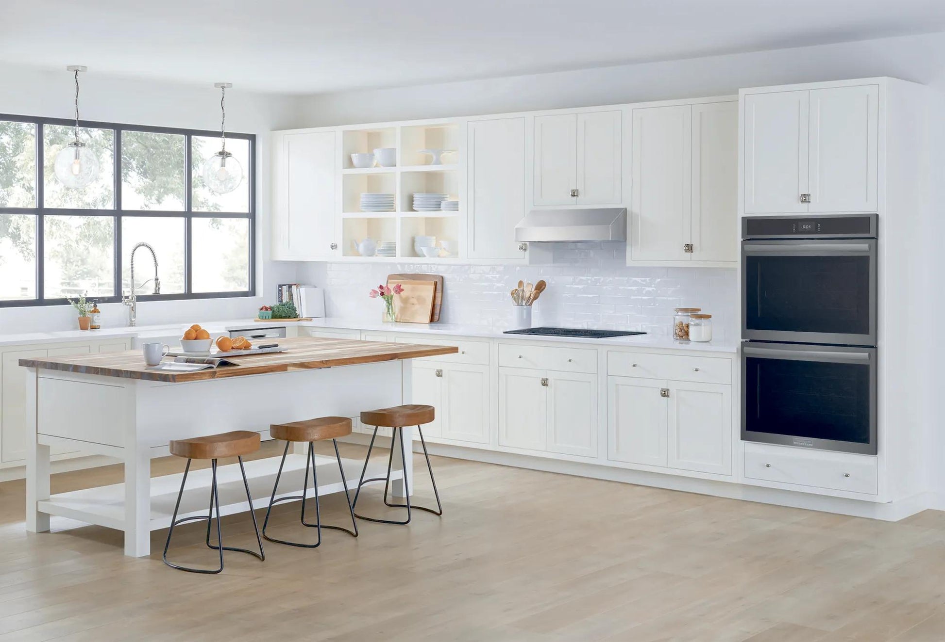 Modern kitchen with white cabinetry and a built-in stainless double wall oven in bright natural light setting