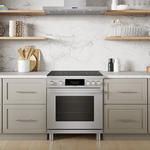 Front view of stainless steel induction freestanding range with ergonomic tilted display and metal knobs in modern kitchen setting