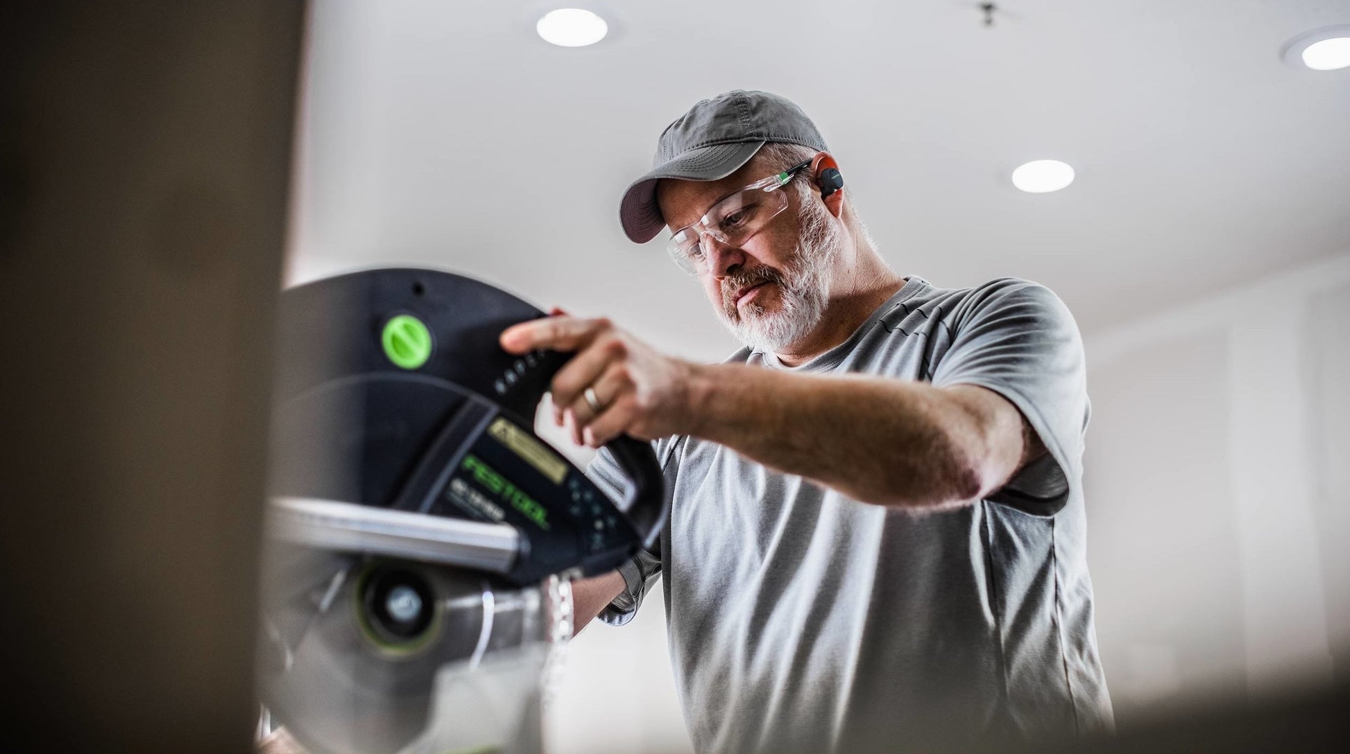 Man wearing Bluetooth hearing protection in a workshop operating a power tool for home improvement and safety use